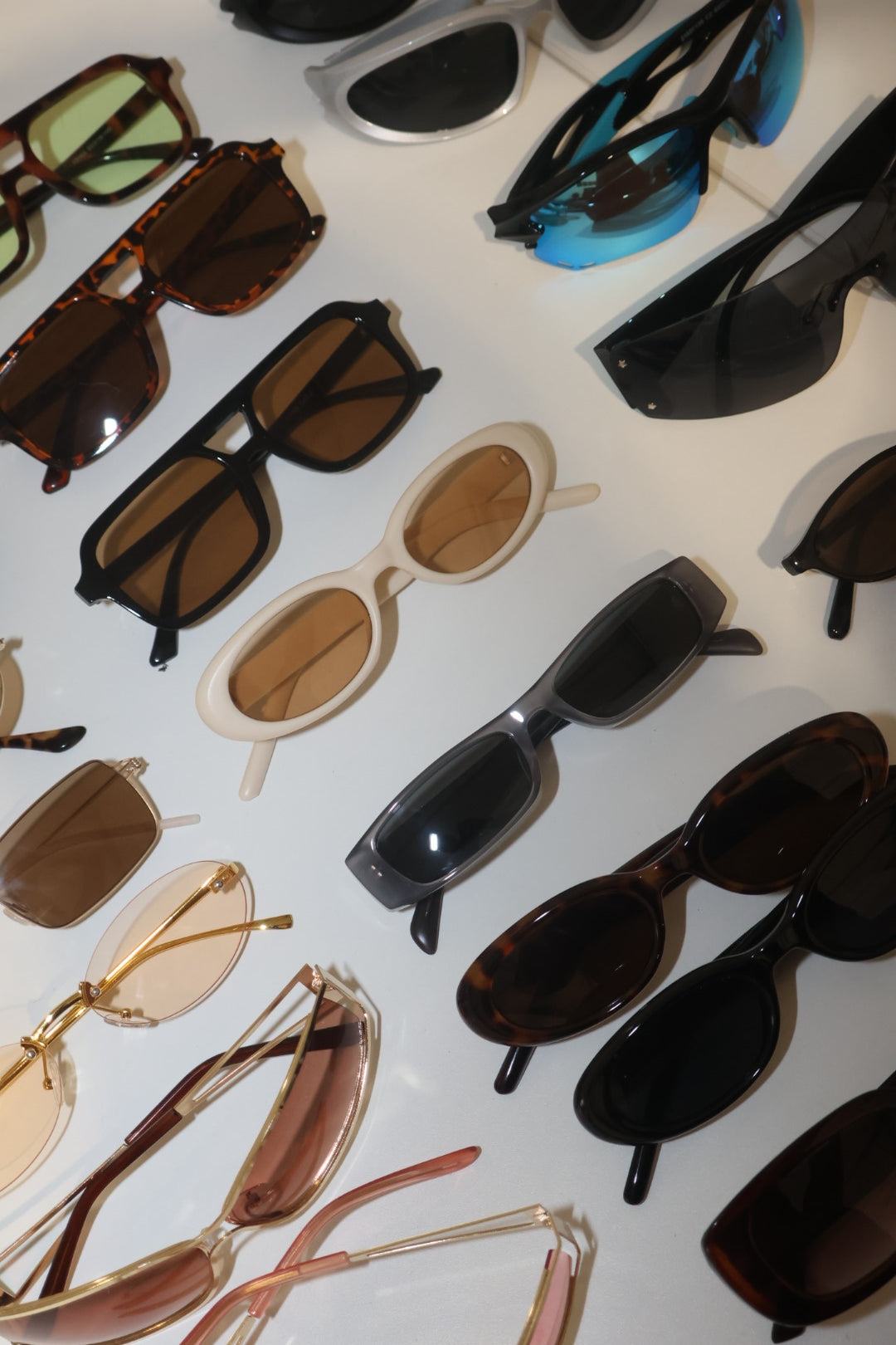 A collection of various sunglasses in different styles, colors, and lens types, arranged on a white surface.