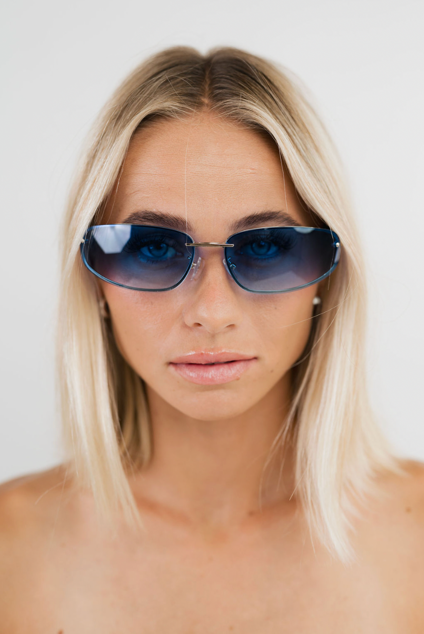 A close-up shot of a blonde woman wearing blue-tinted aviator sunglasses against a plain white background.